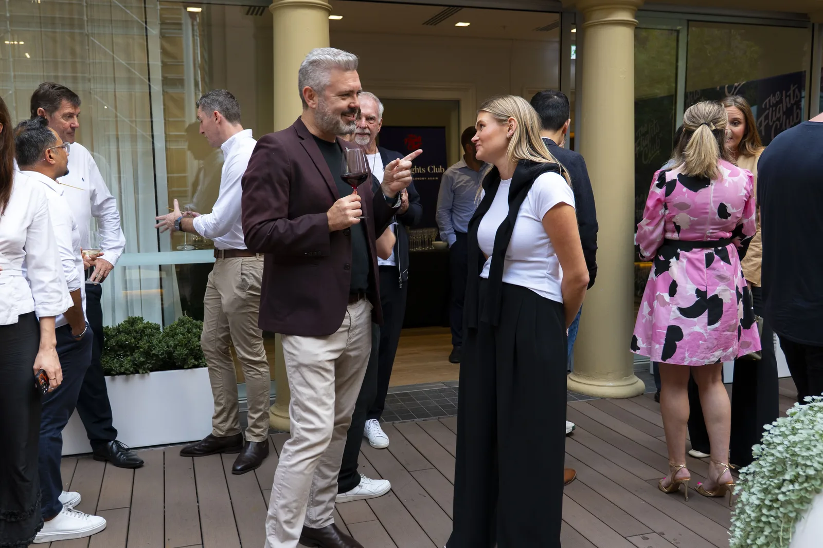 Members' Conversations — two Flights Club members in close conversation on a rooftop terrace, with other members mingling around them.